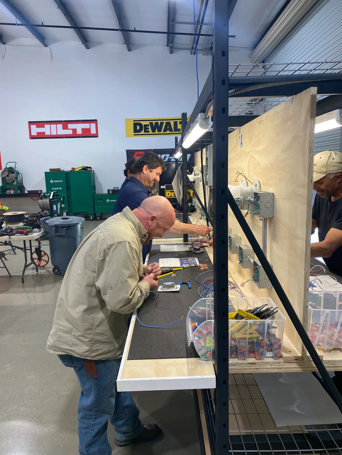 Instructors and students wiring electrical panels in the training facility